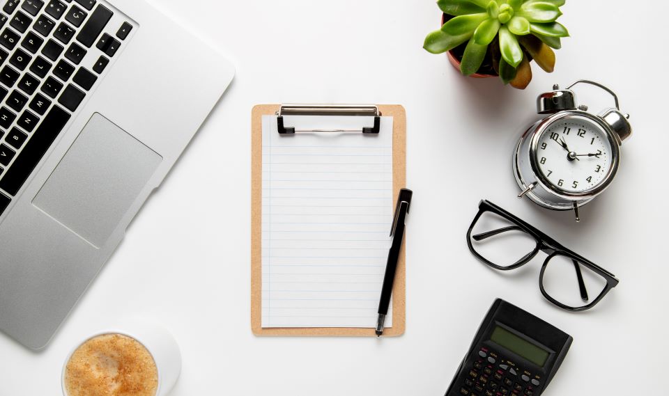 e-öğrenme projesi beyaz zemin üzerinde not kağıdı, kalem, alarmlı saat, gözlük, kahve, hesap makinası, sukulent ve masaüstü bilgisayar.